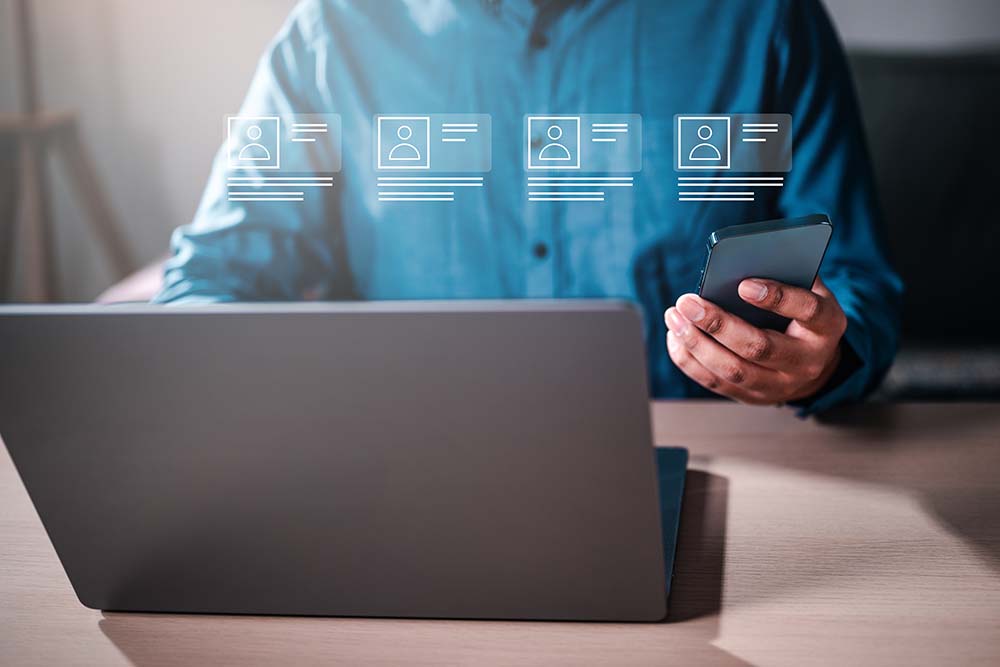 A man is sitting with a laptop and smartphone. shows a employee listing and on premise security, cloud based security employee stats. mobile access control, 1# Toronto Security company, best security company Toronto, experienced security company toronto safelink group, P8MX+GC Brampton, Ontario